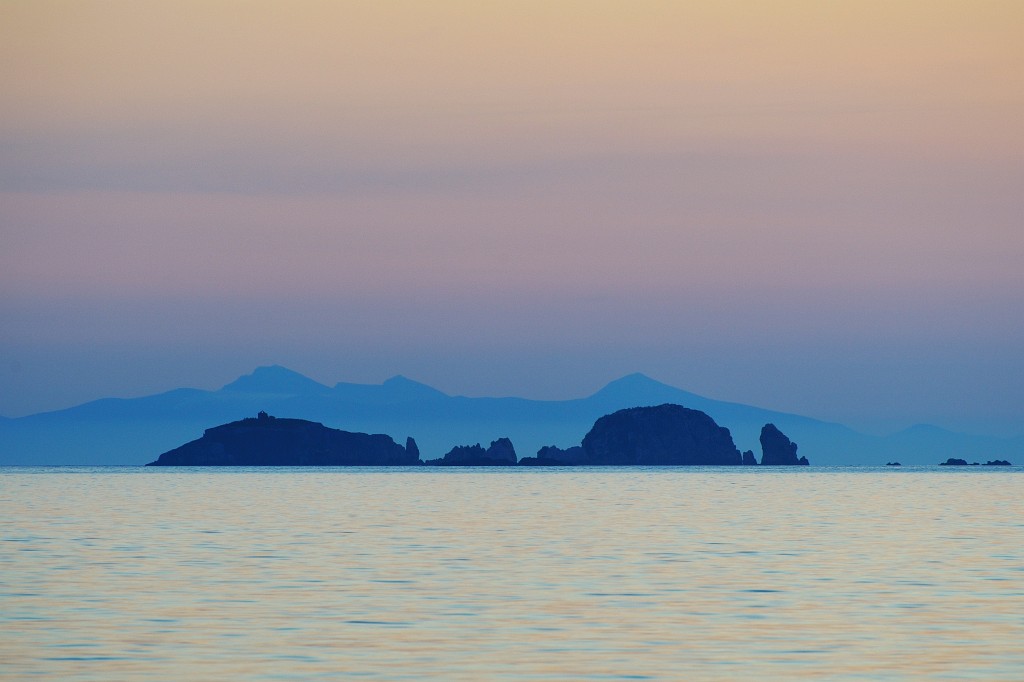 Kykladen-062009-048.jpg - Wieder ist Abend und Dirk und ich versuchen, Nachtaufnahmen im Hafen von Paros zu machen. Durch mein Teleobjektiv sehe ich in der Ferne gestaffelte Inseln im Dunst. Das Meer spiegelt das Orange und Blau des Himmels wieder.